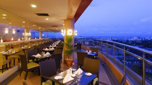 A restaurant with tables set for dining, a potted plant, and a view of the cityscape. - Borneo Royale Hotel (Tawau)