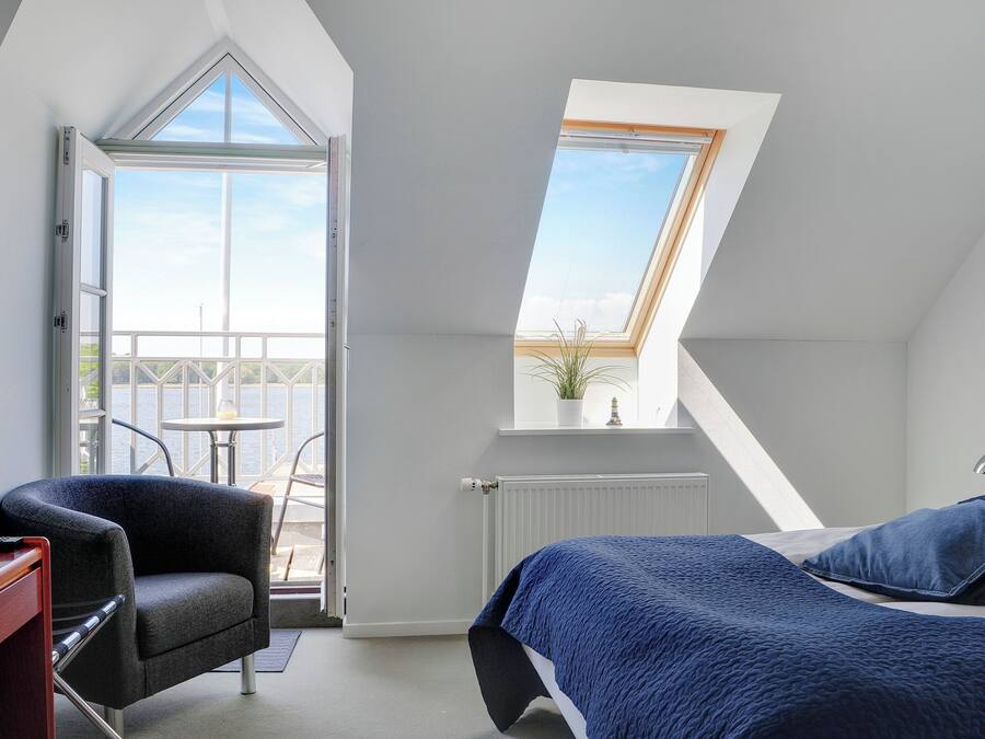 Un dormitorio con tragaluz, una cama con ropa de cama azul, una silla y vistas al exterior.
