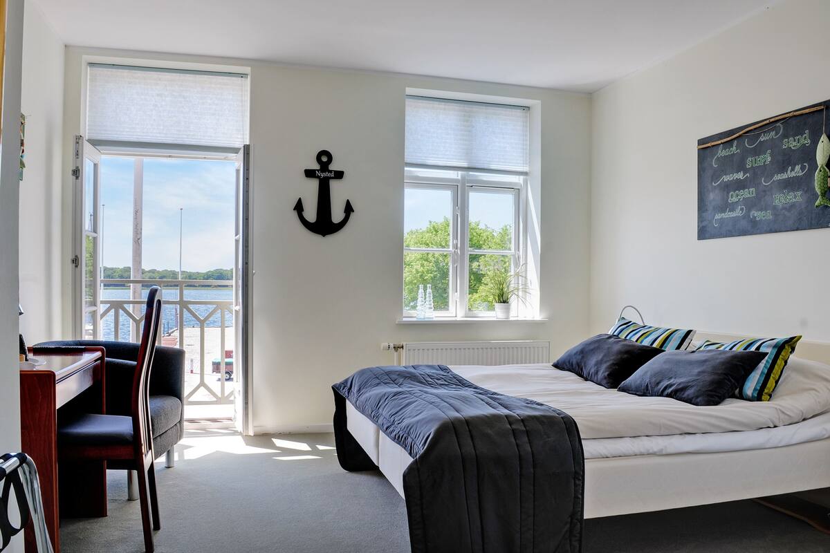 A bedroom with a bed, a desk, and a chair. There is a window with a view of the outdoors.