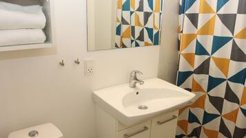 Een badkamer met een witte wastafel, een spiegel, een toilet en een douchegordijn met een geometrisch patroon.