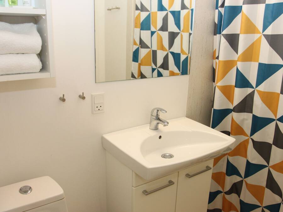 Een badkamer met een witte wastafel, een spiegel, een toilet en een douchegordijn met een geometrisch patroon.