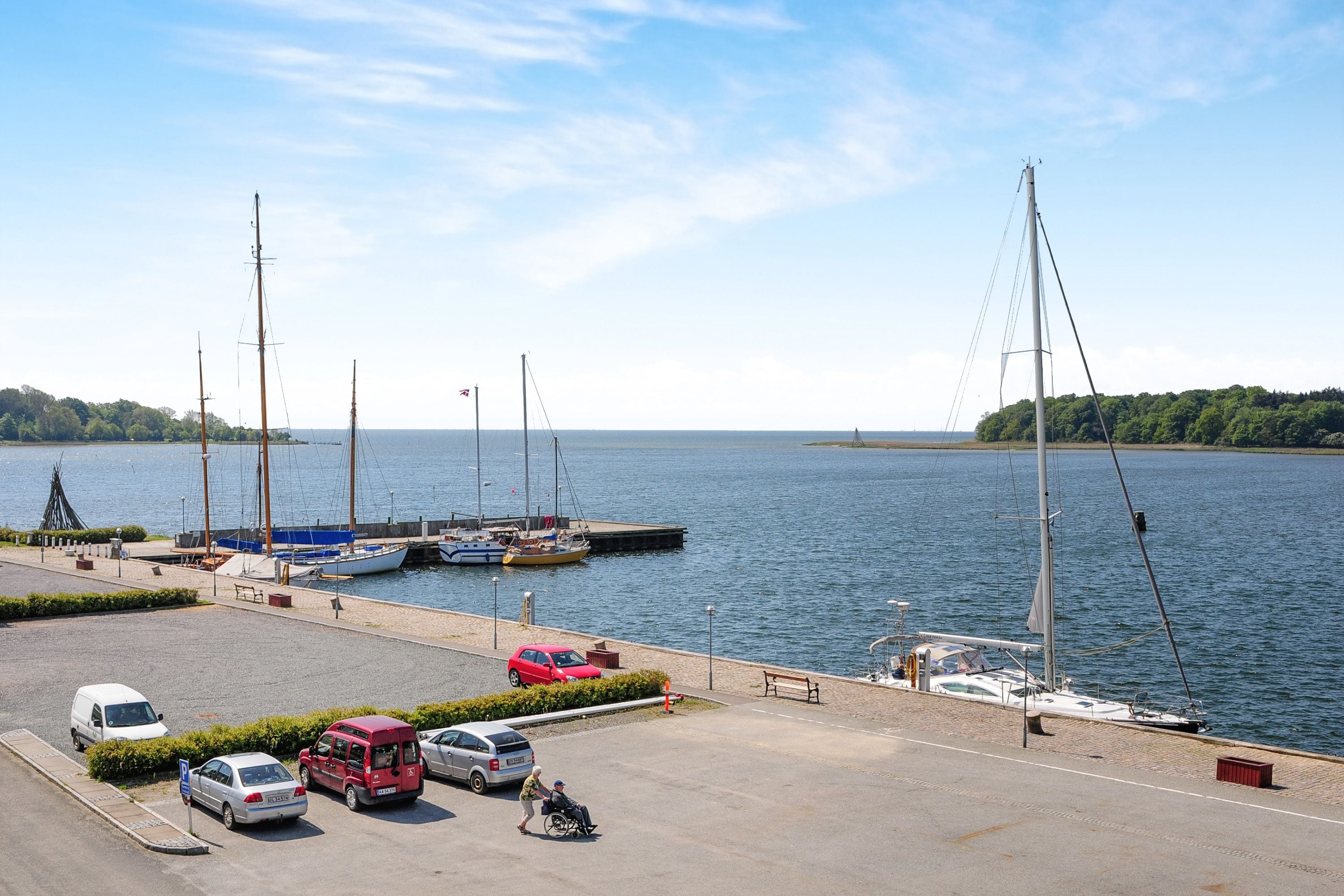 A marina with boats docked, a parking area with cars, and a clear view of the water.