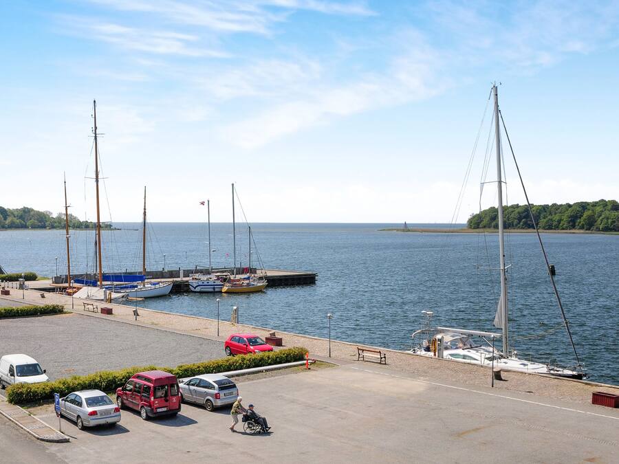 A marina with boats docked, a parking area with cars, and a clear view of the water.