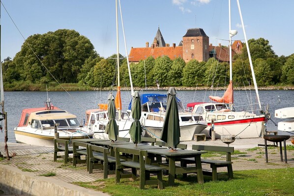A marina with several sailboats docked, wooden benches, and a castle in the background. - Hotel Nysted Havn (Nysted)