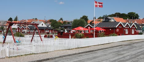 Un edificio rojo con cerca de piquetes blancos, una bandera y un parque infantil.