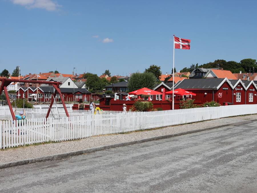 Un edificio rojo con cerca de piquetes blancos, una bandera y un parque infantil.