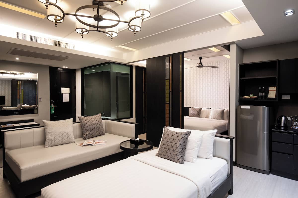 A modern hotel room with a bed, sofa, and a small kitchenette.