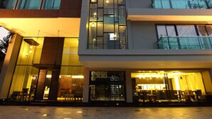 A multi-story hotel with a modern design, featuring a prominent glass facade and a central entrance. - De Chai Oriental Nimman (Chiang Mai)