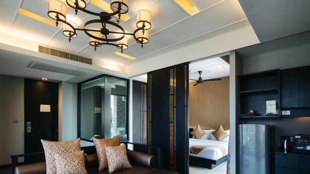 A modern hotel room with a sofa, coffee table, and a kitchenette. - De Chai Oriental Nimman (Chiang Mai)