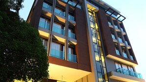 A multi-story hotel with a modern design, featuring a glass facade, multiple balconies, and a well-lit entrance area. - De Chai Oriental Nimman (Chiang Mai)