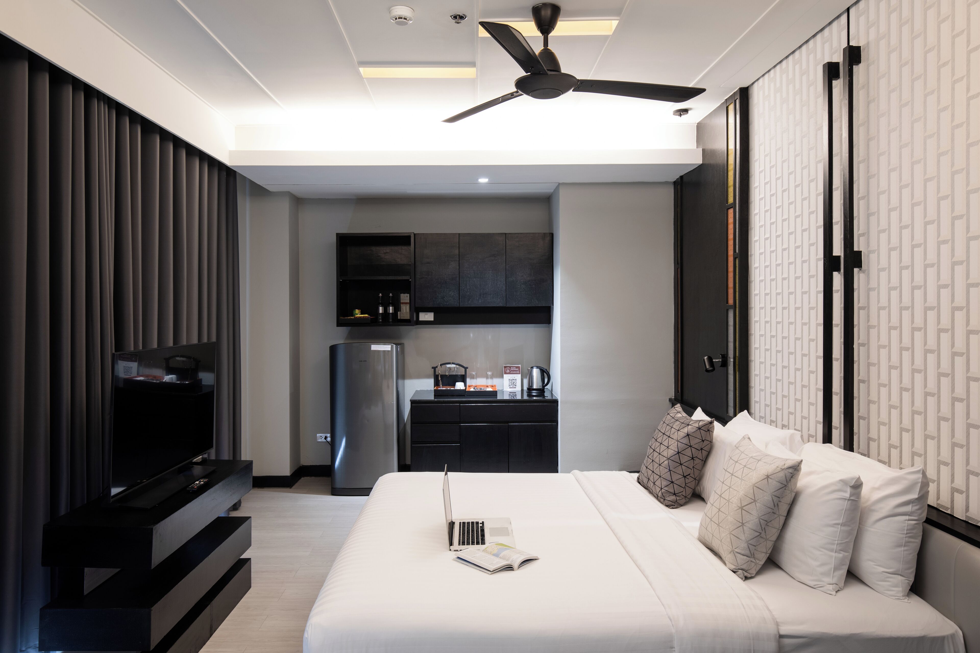 Una moderna camera d'albergo con un letto, una TV, un portatile e un angolo cottura sullo sfondo.