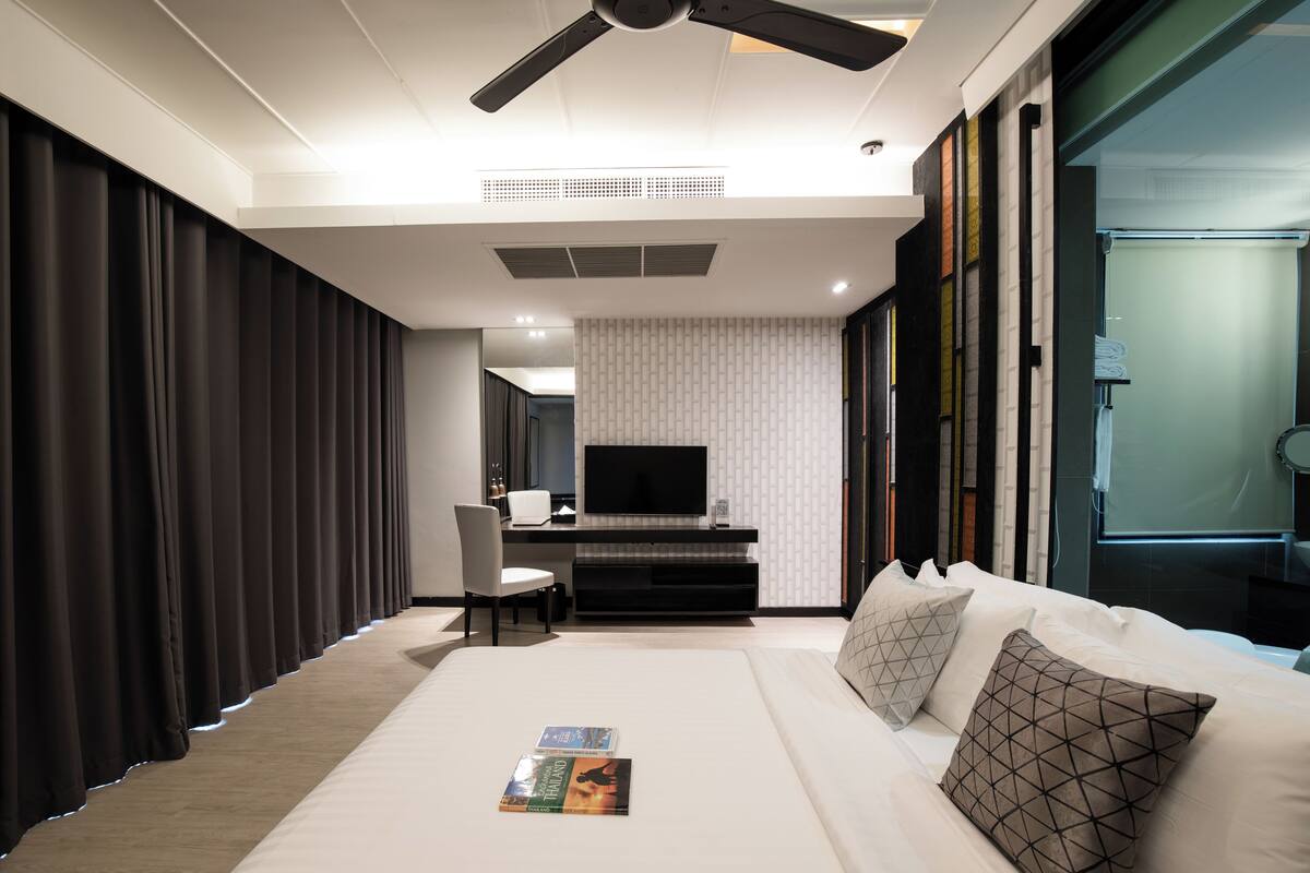 A modern hotel room with a bed, a desk with a TV, and a large window.