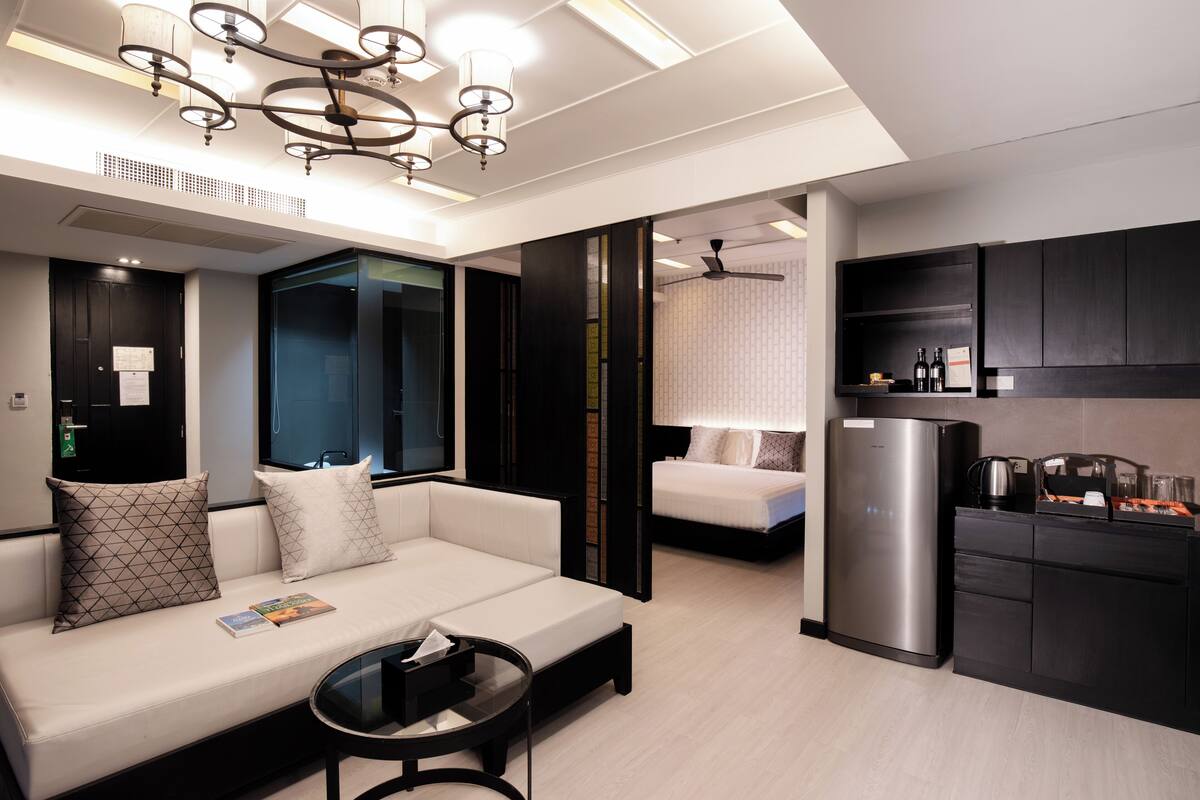 A modern hotel room with a sofa, a coffee table, a refrigerator, and a kitchen area with cabinets and a microwave.