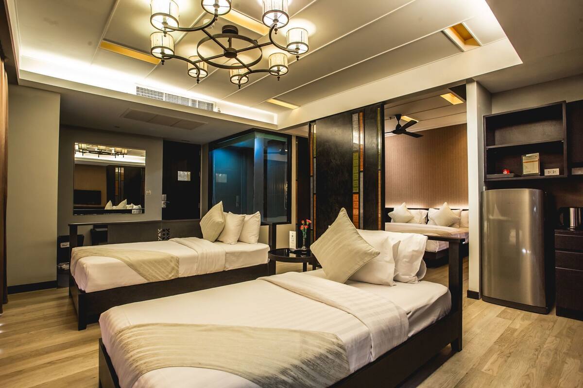 A hotel room with two beds, a large mirror, a minibar, and a ceiling fan.