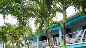 A hotel with a blue exterior, a balcony with white railings, and lush greenery including palm trees and pink bougainvillea flowers. - Island Club Turks (Providenciales)