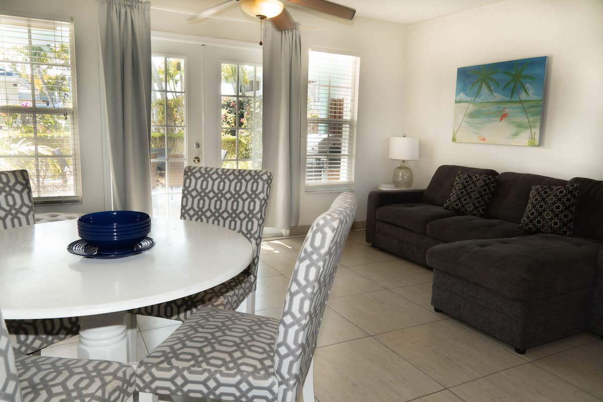 A living room with a round table, patterned chairs, a dark sofa, and a painting of a beach scene.