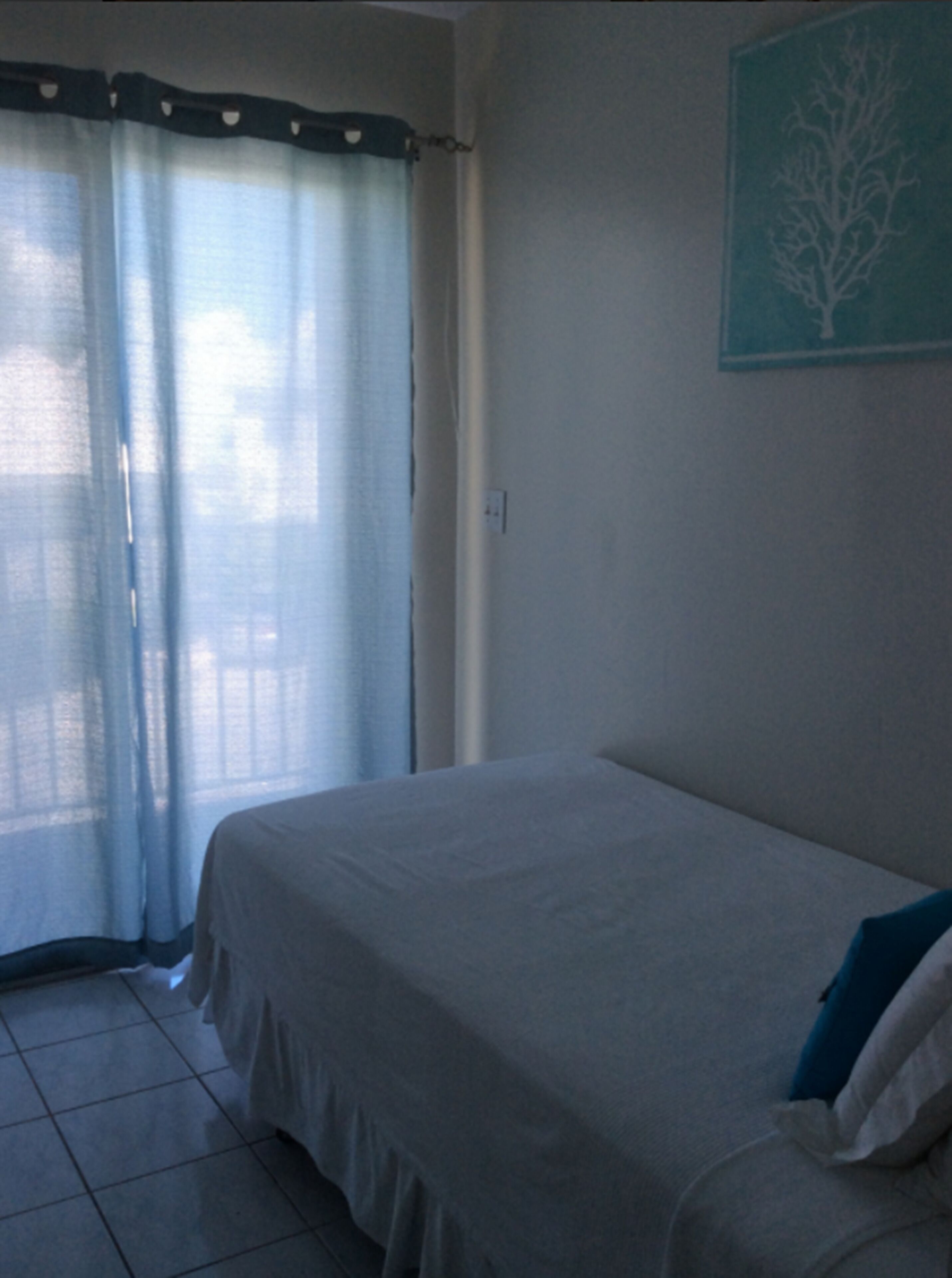 Un dormitorio con cama, una ventana con cortinas translúcidas y una obra de arte colgada en la pared.