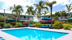 A swimming pool with lounge chairs and umbrellas, surrounded by palm trees and tropical plants. - Island Club Turks (Providenciales)