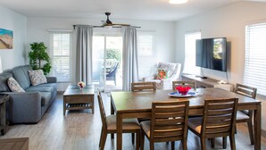 A modern living room with a dining area, including a wooden table and chairs, a sofa, and a television. - Island Club Turks (Providenciales)