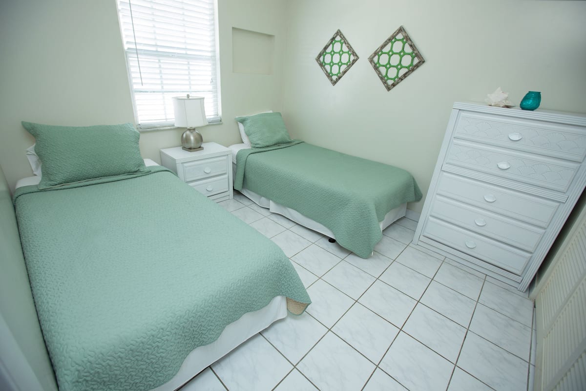 A bedroom with two beds, white nightstands, a dresser, and decorative wall art.