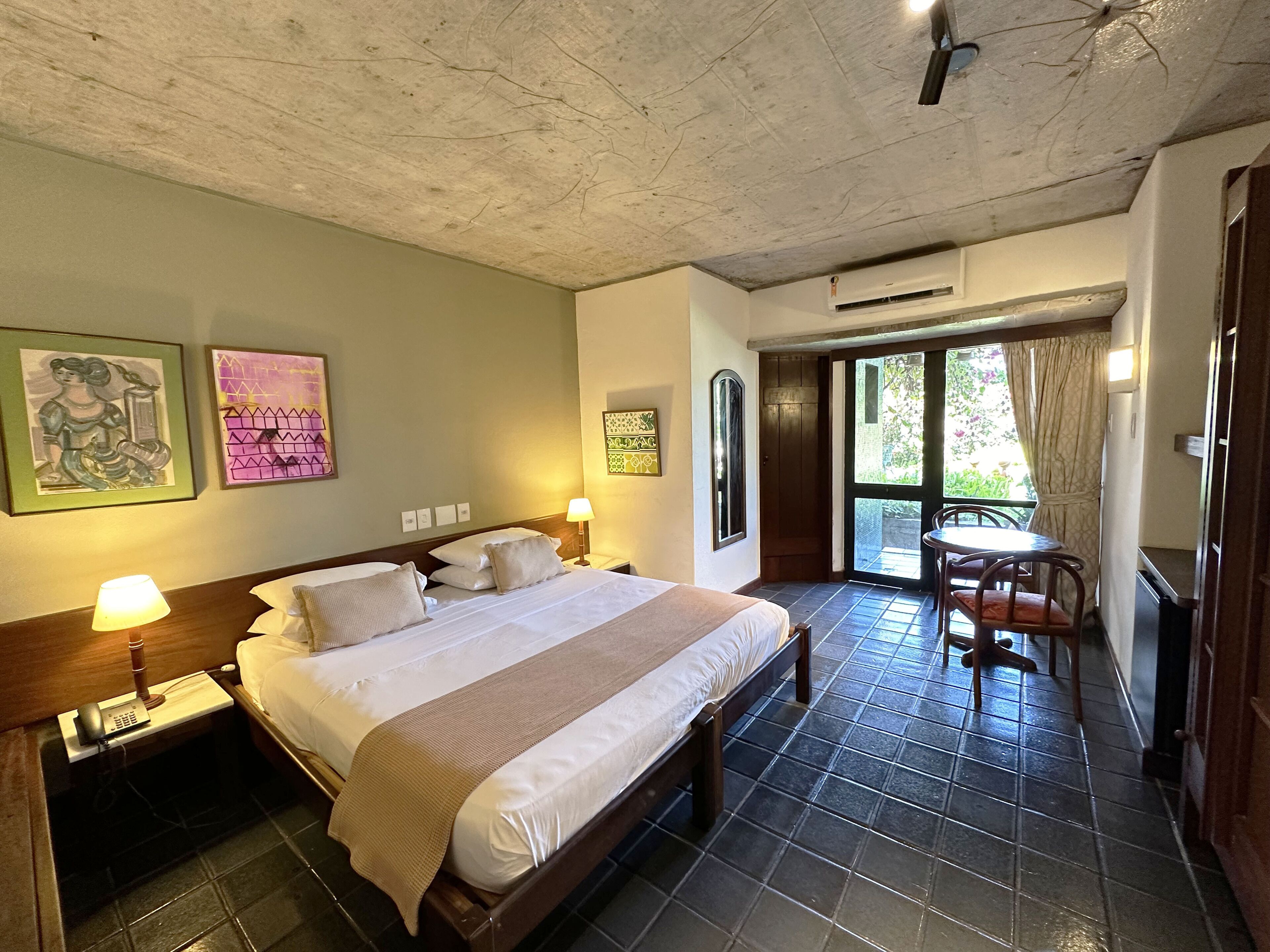 Ein Hotelzimmer mit einem großen Bett, Nachttischlampen, einem kleinen Tisch mit Stühlen und Bildern an den Wänden.