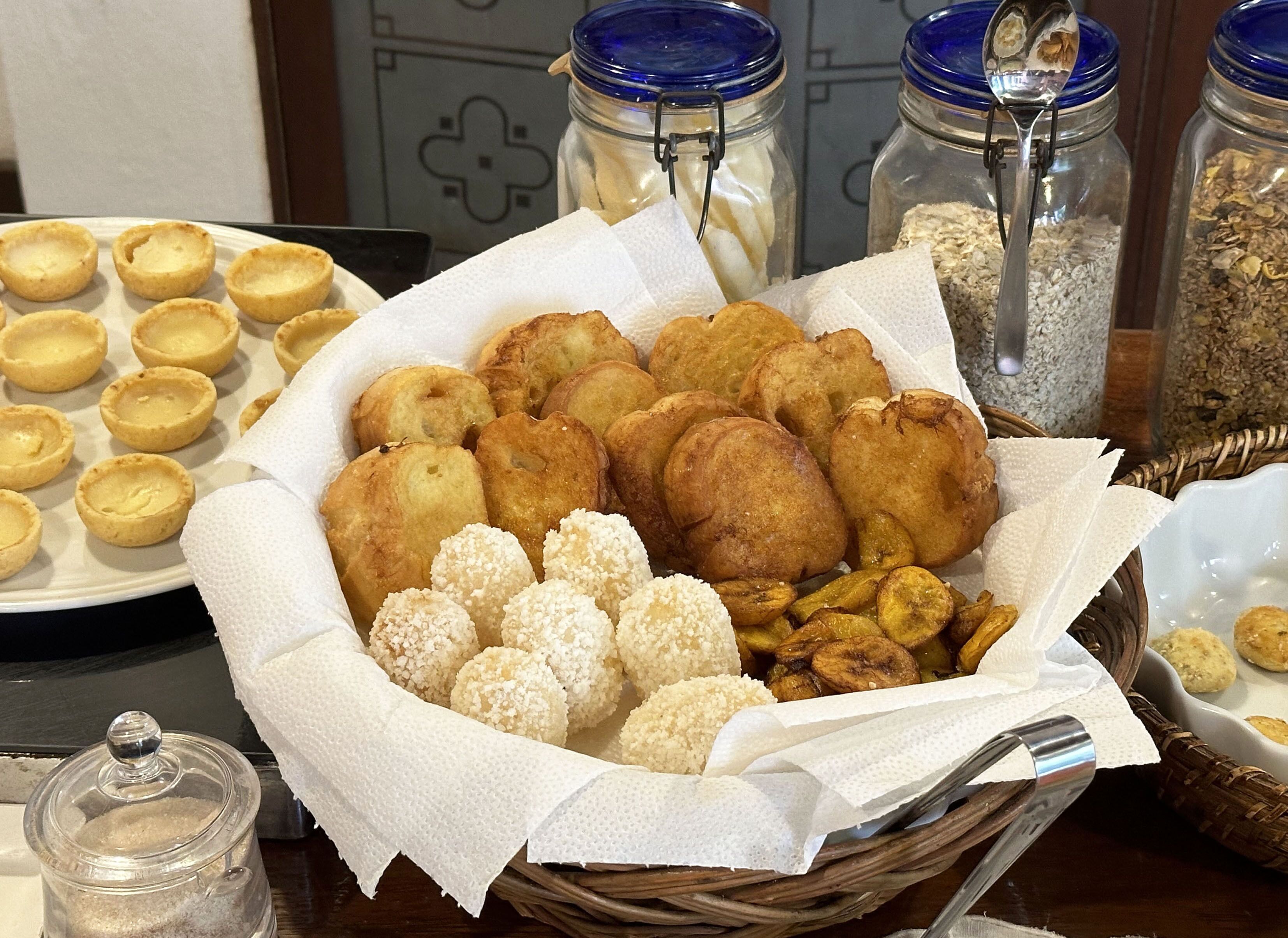 A basket of assorted fried snacks, including fritters and small cakes, on a table.
