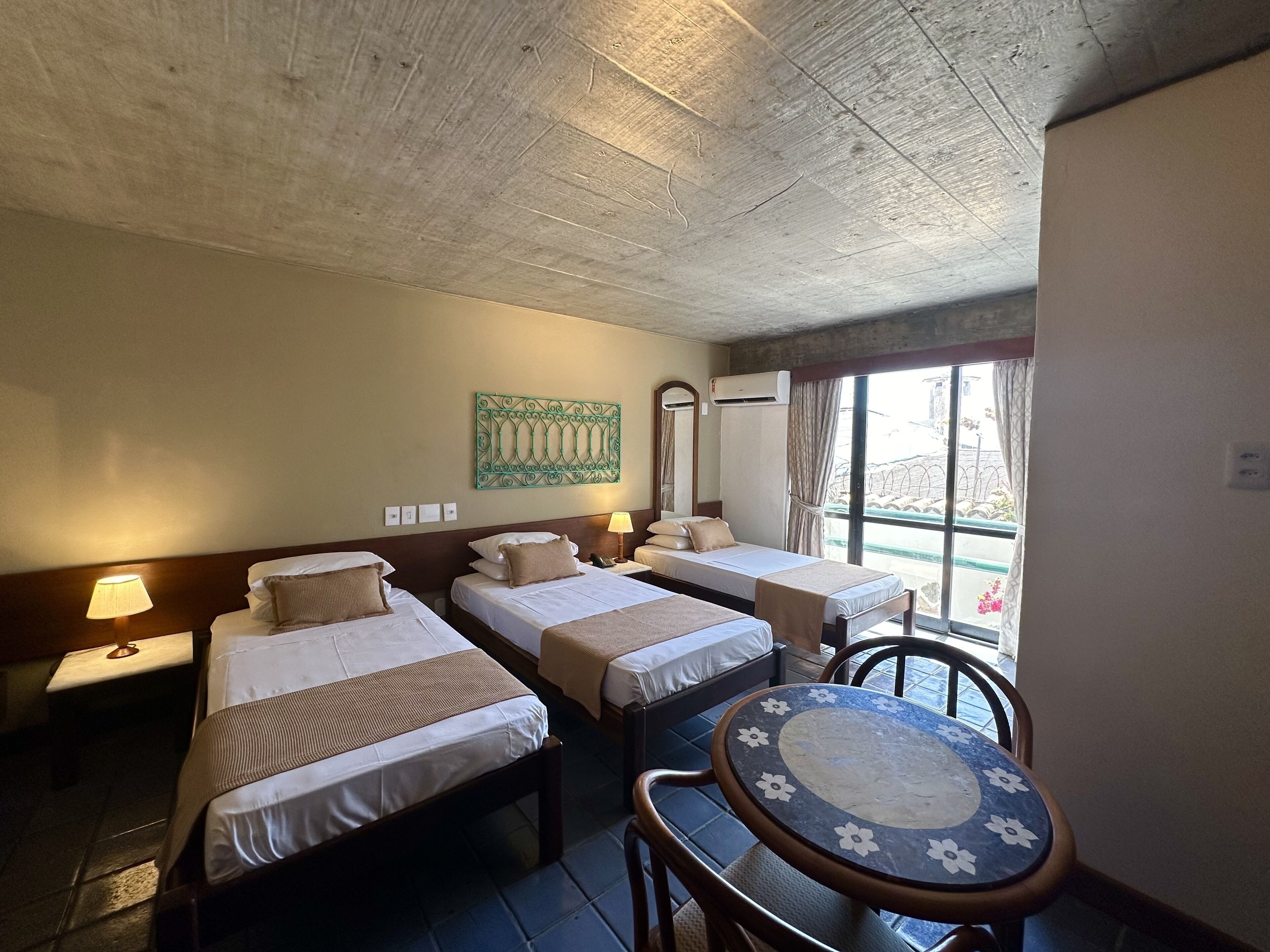 A hotel room with two single beds, a small round table, and a window with curtains.
