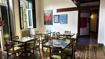 A dining area with a glass-top table surrounded by wooden chairs with green cushions, a tiled floor with a floral pattern, and artwork on the walls.