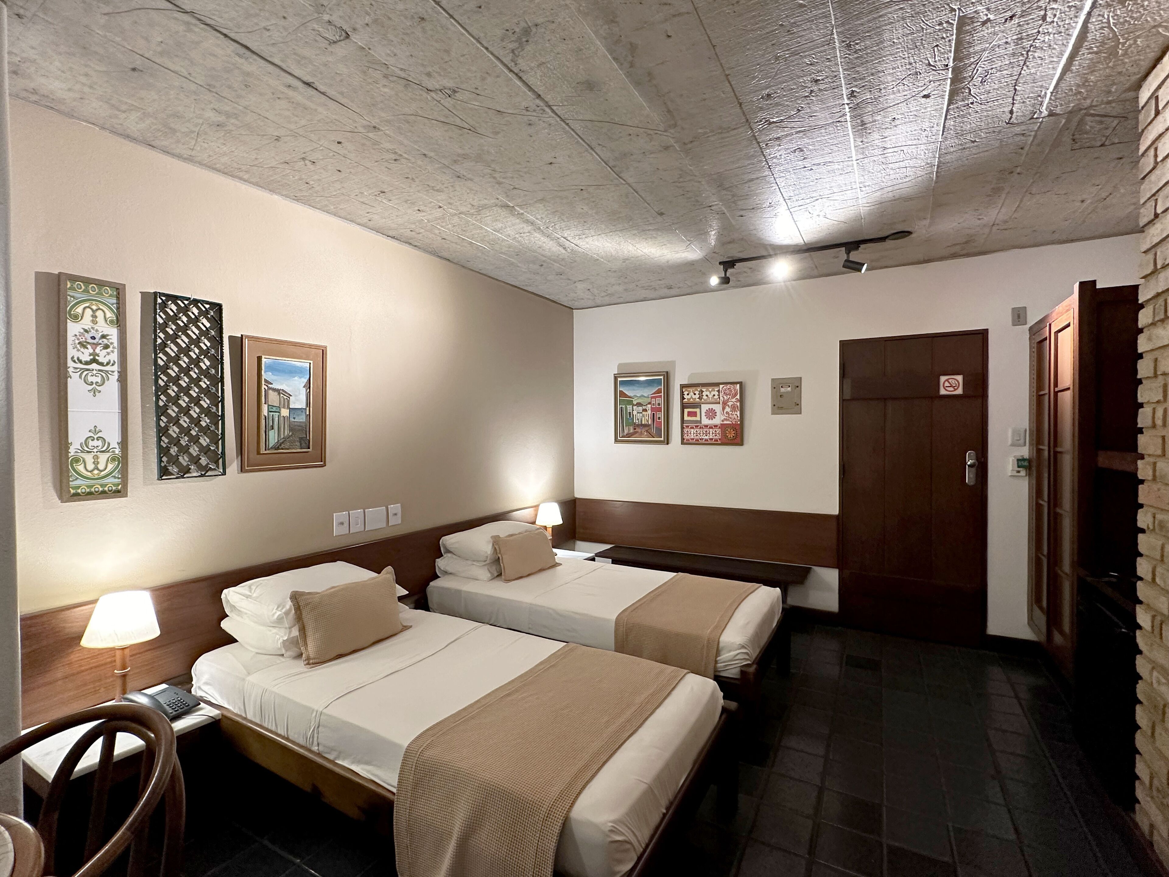 Habitación de hotel con dos camas, un escritorio, una silla y cuadros en las paredes.