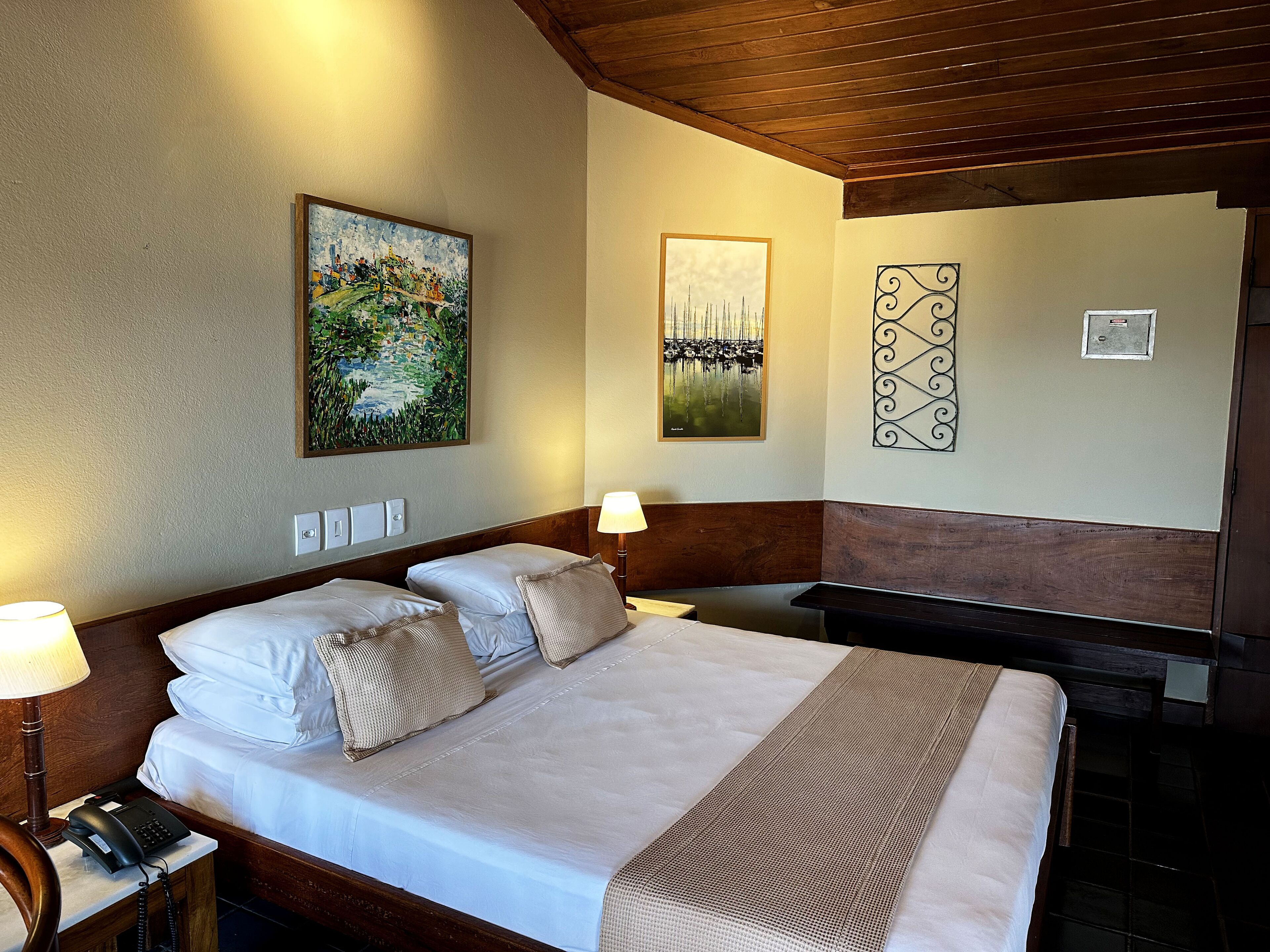 A hotel room with a large bed, a desk, a lamp, and artwork on the walls.