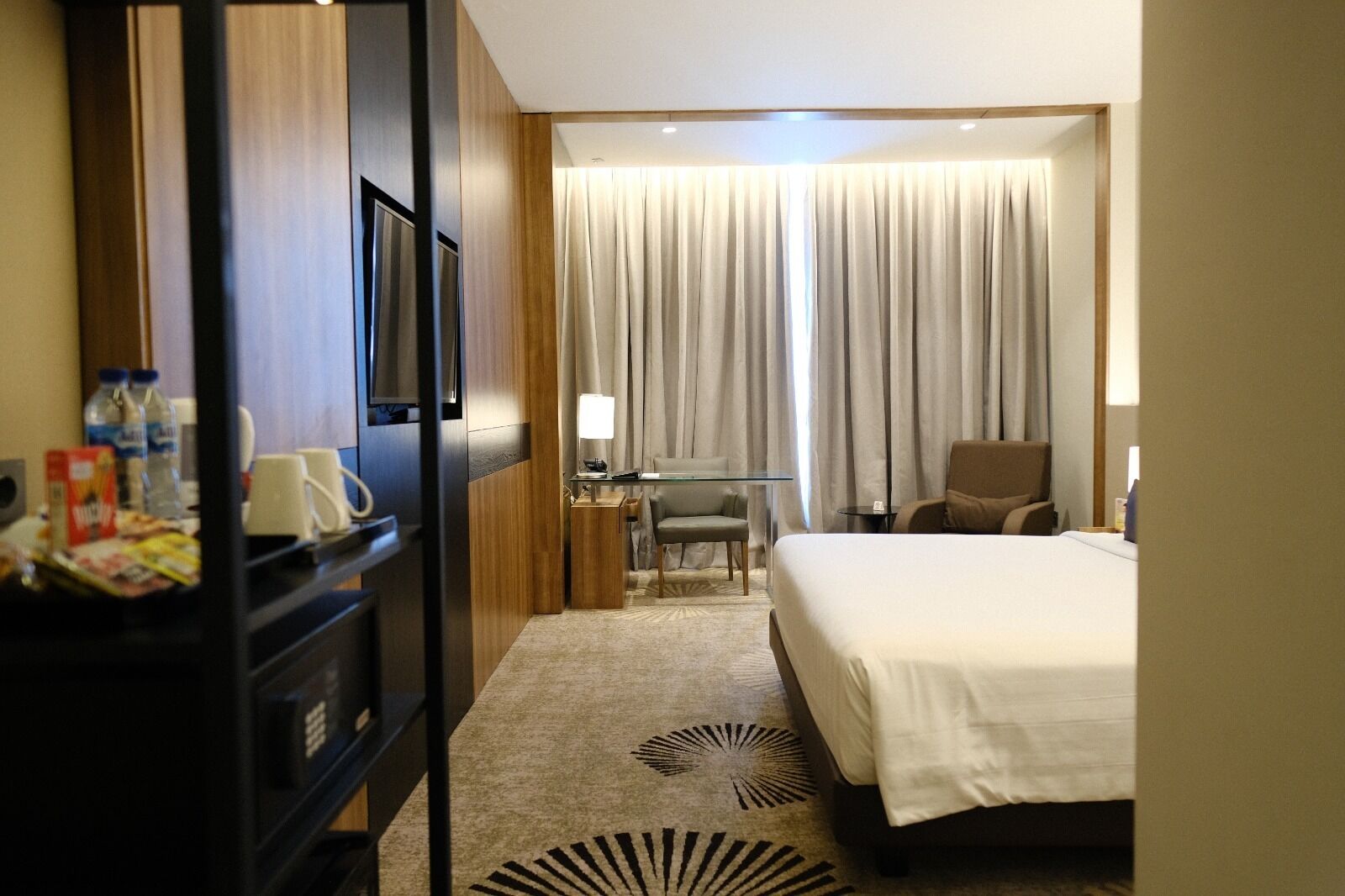 Ein Hotelzimmer mit Bett, Schreibtisch, Stuhl, Fernseher und einem fensterbepflanzten Fenster.