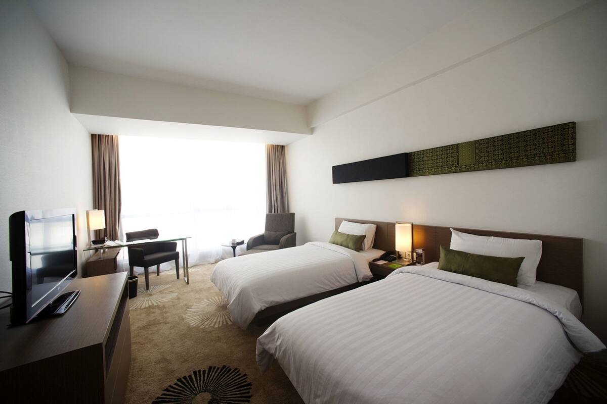 Ett hotellrum med två sängar, ett skrivbord med en tv, en stol och ett fönster med gardiner.