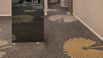 Un pasillo moderno con un pilar reflectante, suelos alfombrados con un diseño en forma de sol y un largo corredor que conduce a una puerta.