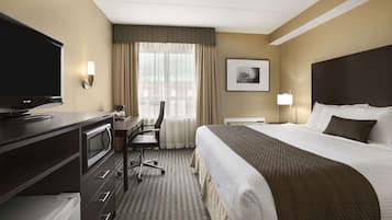 A hotel room with a bed, a desk with a television, a chair, a desk lamp, and a picture on the wall.