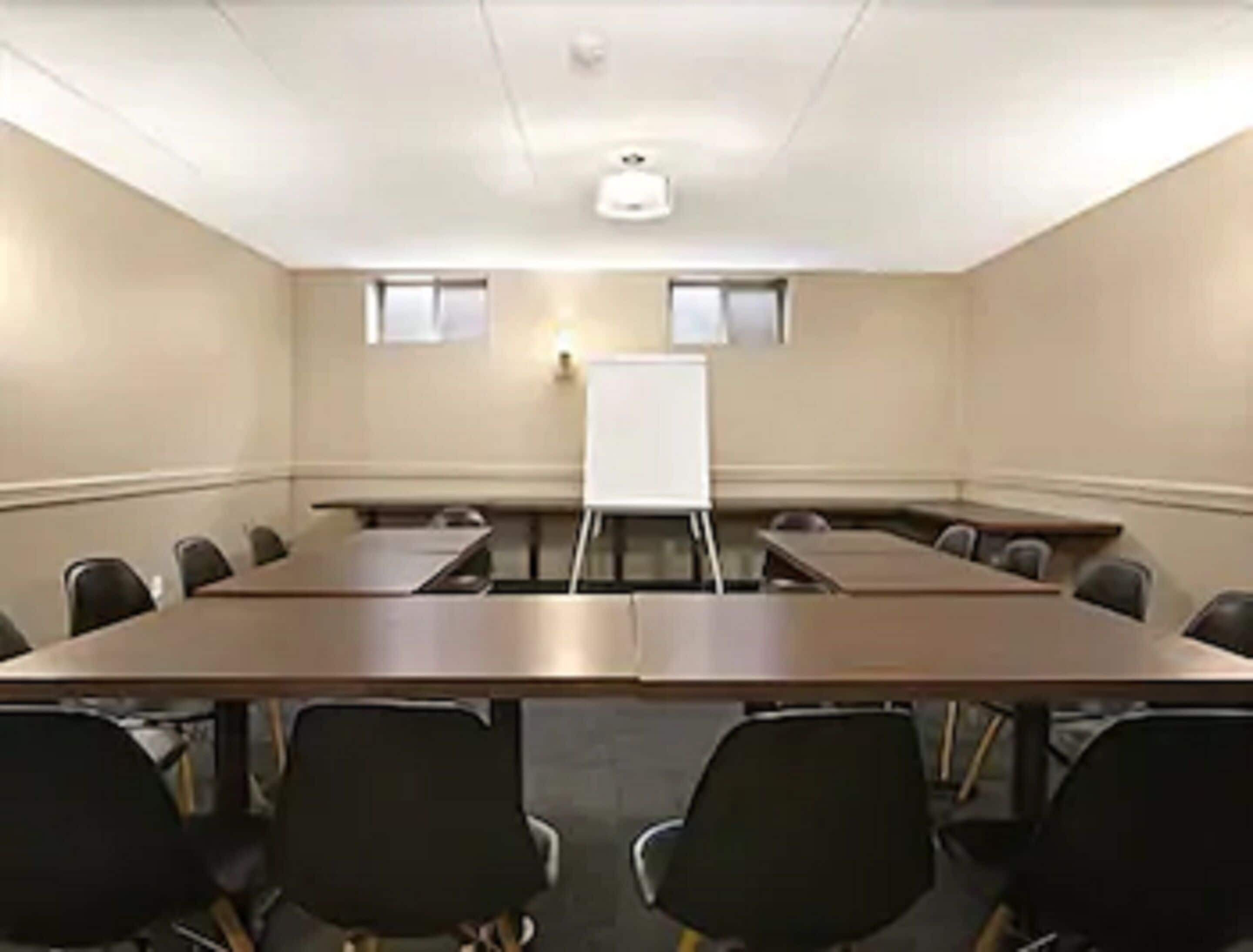 A conference room with a long table, several chairs, a whiteboard, and two windows.
