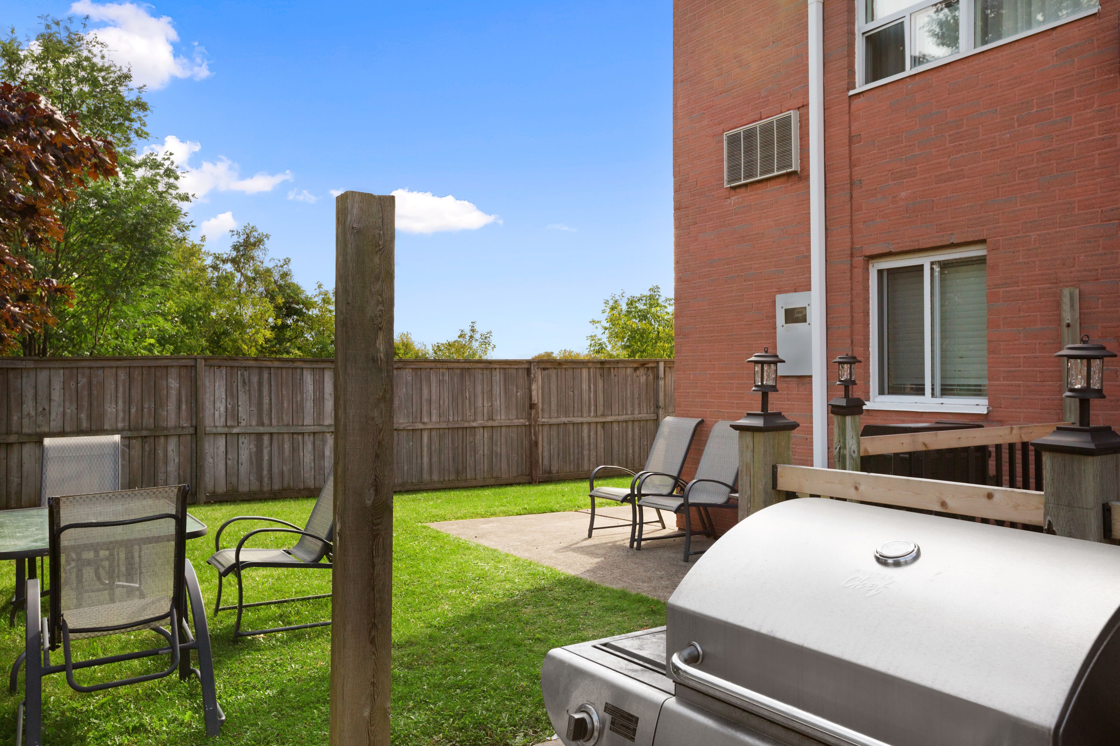 An outdoor patio with a grill, chairs, and a wooden fence.