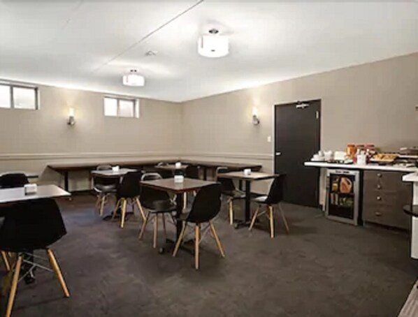 A conference room with tables and chairs, a kitchenette, and a door.