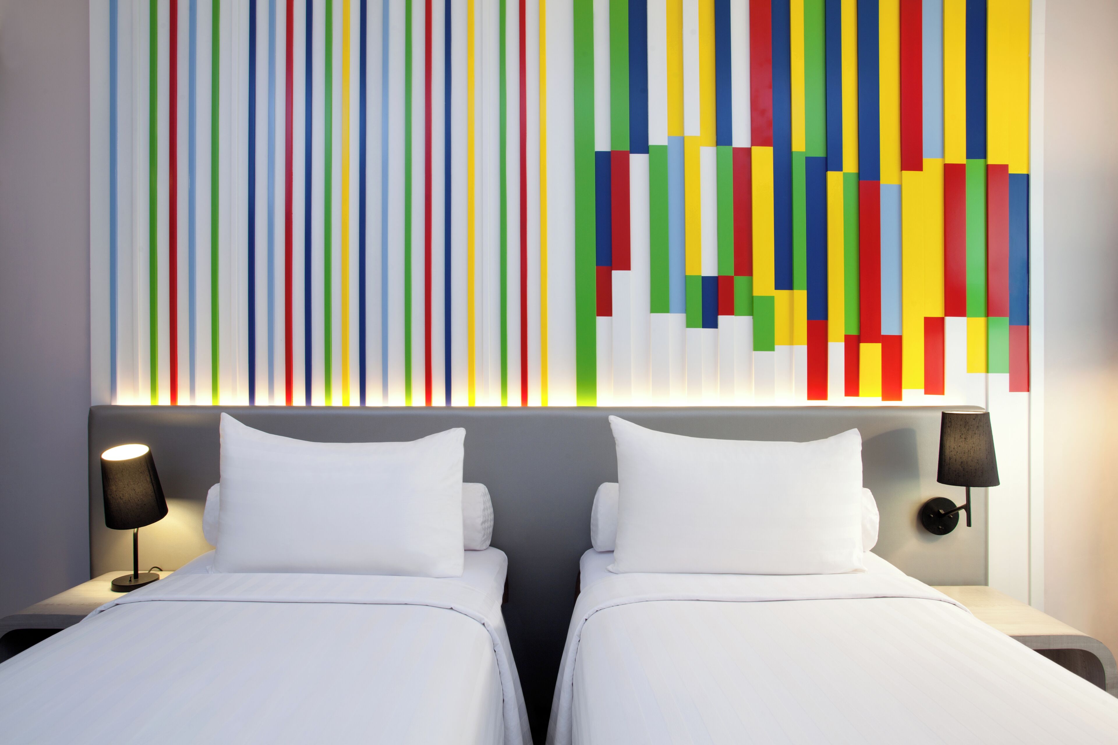 A hotel room with two beds, a modern wall art piece, and a nightstand with a lamp.