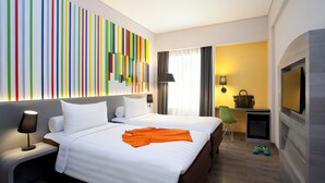 Una habitación de hotel con una cama grande, un escritorio con silla, un televisor y una obra de arte de colores en la pared.