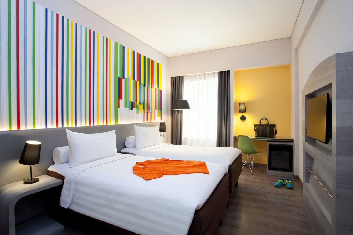 A hotel room with a large bed, a desk with a chair, a TV, and a colorful wall art piece.