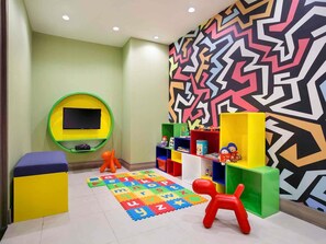 Zona de juegos infantiles con fichas del alfabeto, juguetes y un llamativo diseño de pared geométrico.