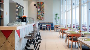 Un restaurante moderno con zona de bar, techos altos y ventanales amplios.