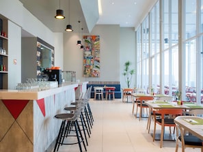 A modern restaurant with a bar area, high ceilings, and large windows. - ibis Styles Jakarta Mangga Dua Square (Jakarta)
