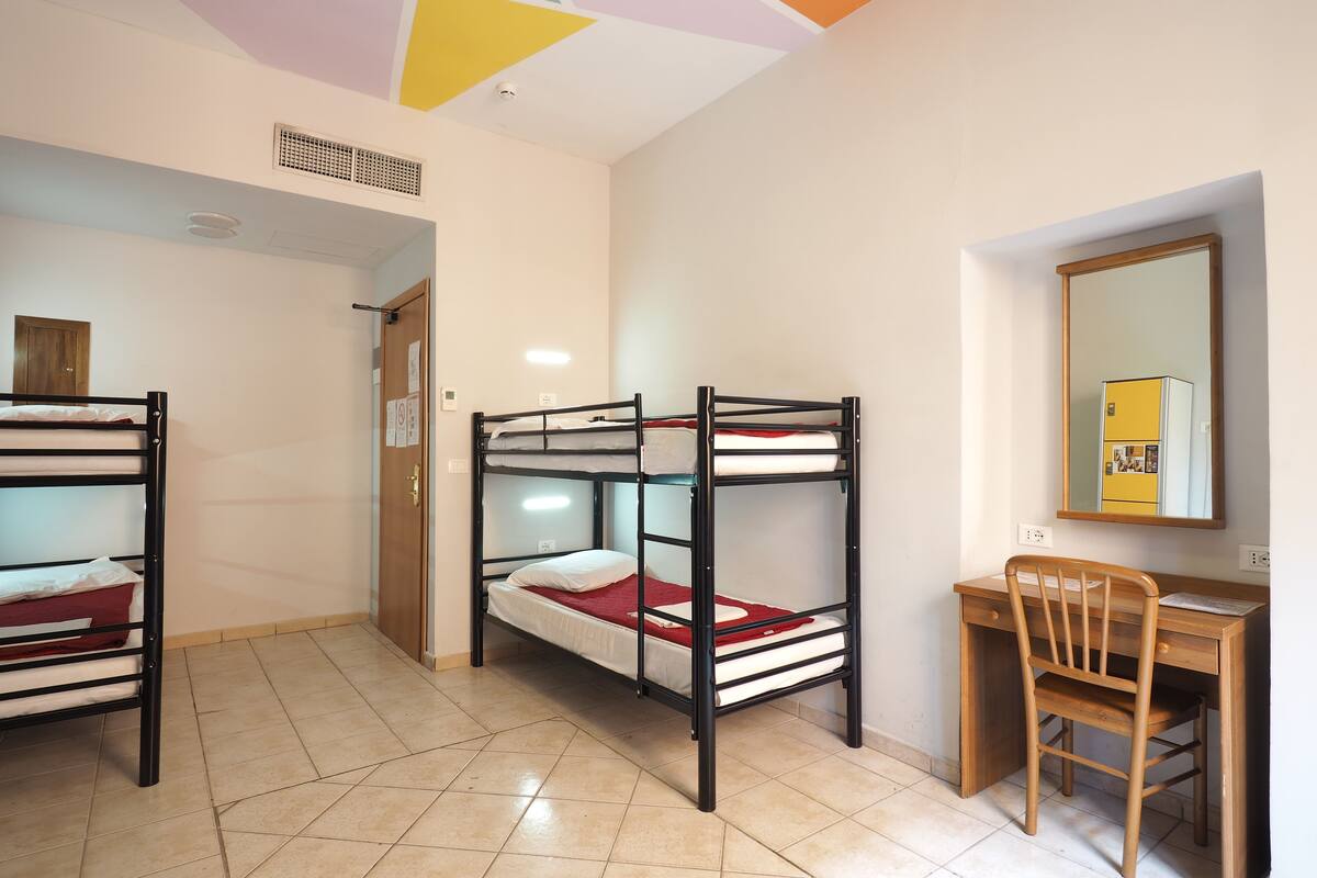A dormitory room with bunk beds, a desk, and a chair.