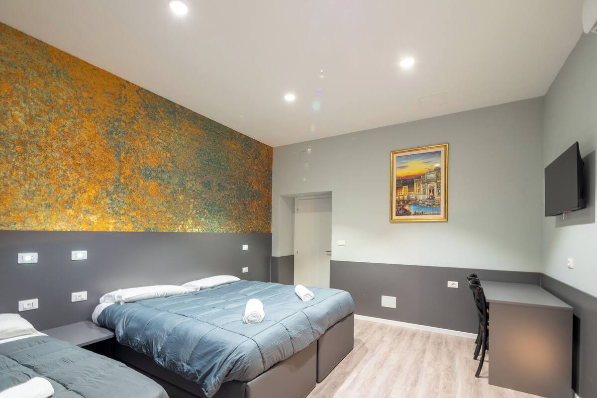 A modern hotel room with a large bed, a desk, and a painting on the wall.