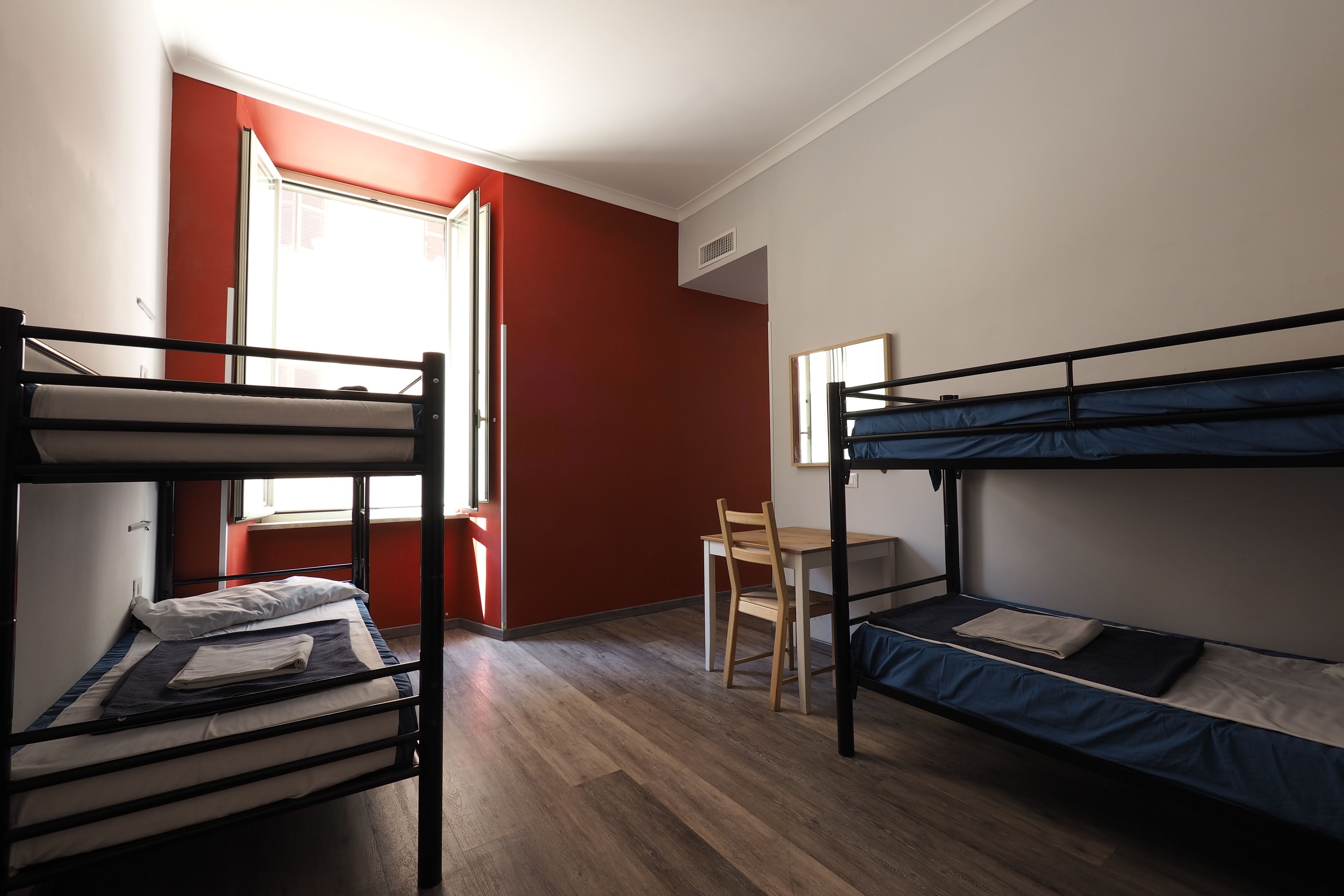 A dormitory room with two bunk beds, a wooden desk, and a chair.