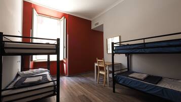 A dormitory room with two bunk beds, a wooden desk, and a chair.