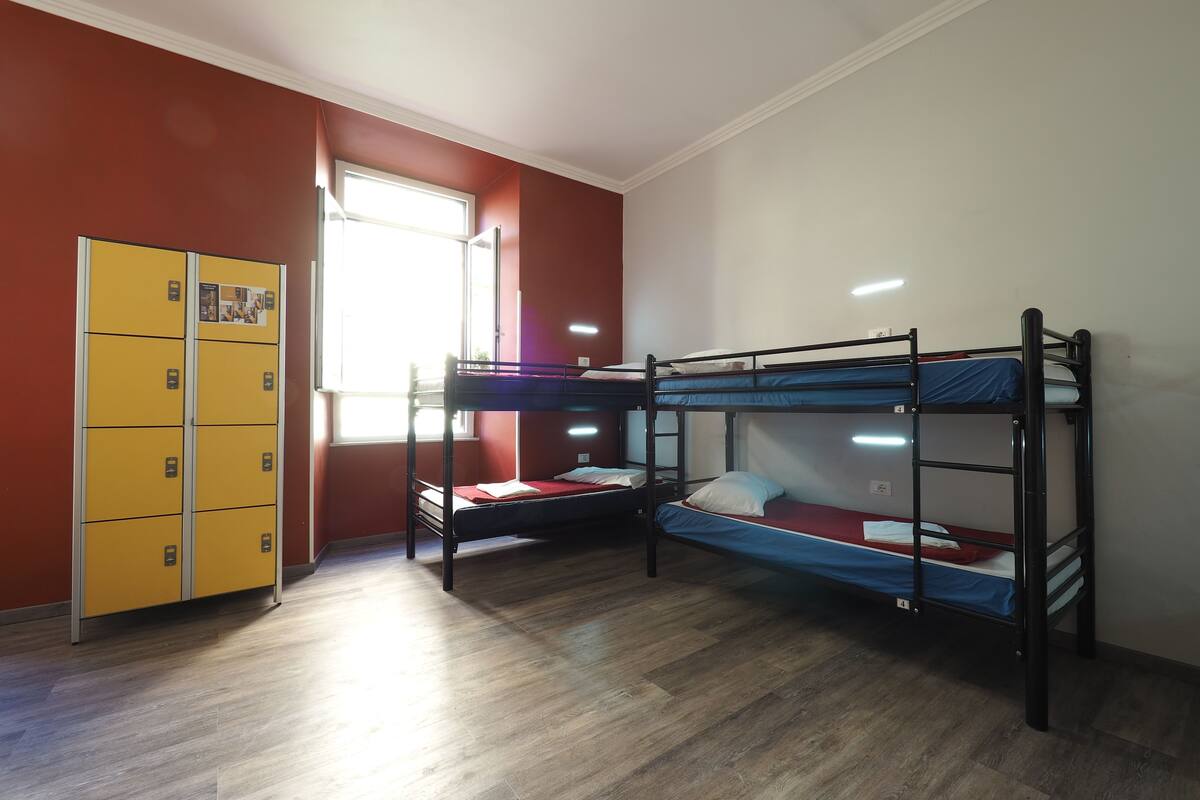 A dormitory room with two bunk beds, a yellow storage unit, and a window providing natural light.