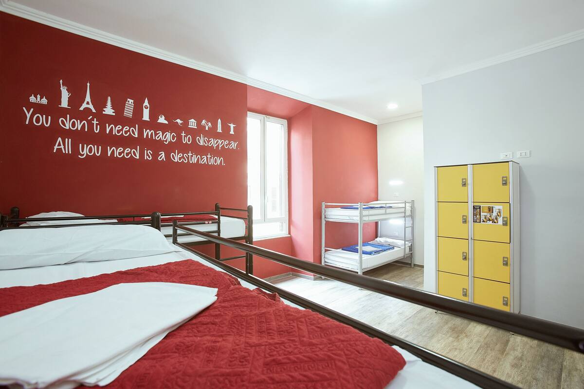 A dormitory room with bunk beds, a red wall with a motivational quote, a window, and a yellow storage unit.