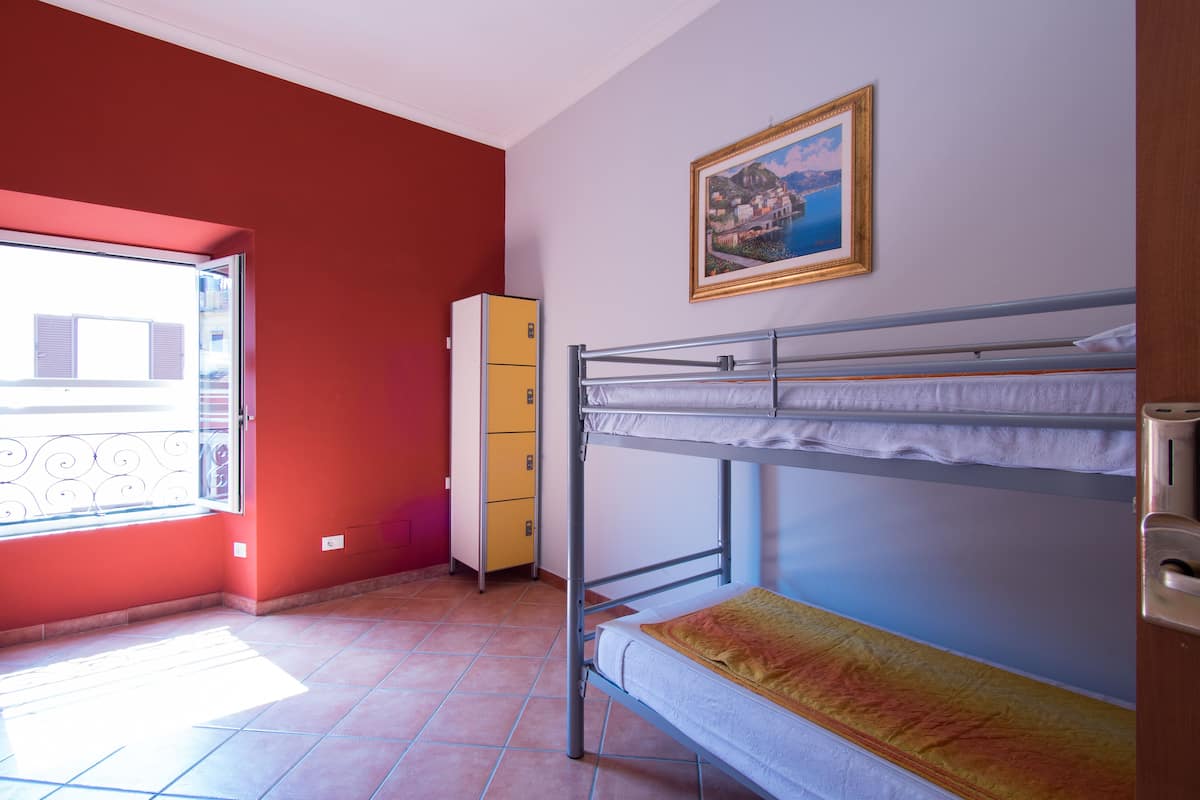 A room with a bunk bed, a window with a view, a yellow cabinet, and a framed picture on the wall.
